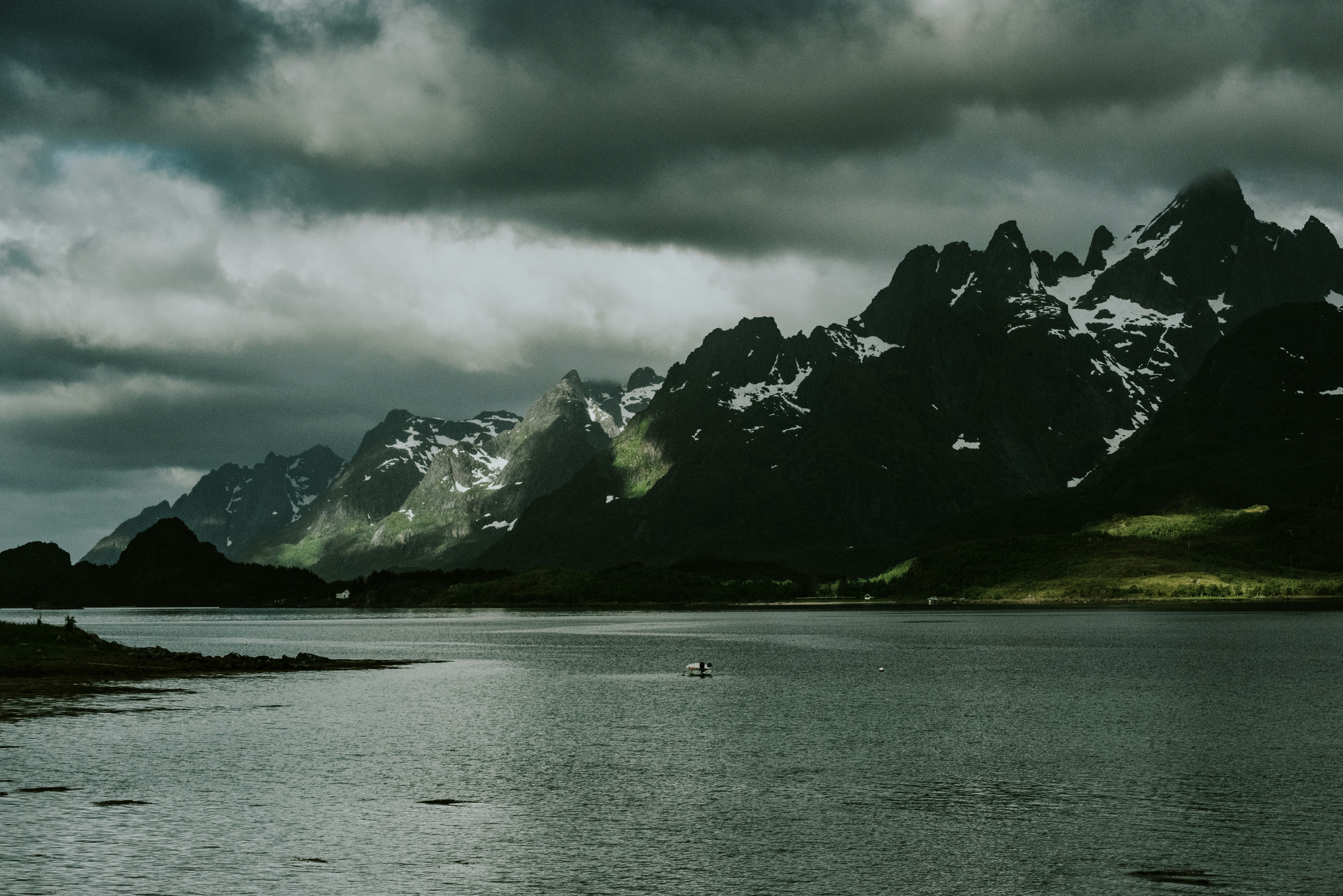 boat on sea near mountain under cloudy sky during daytime